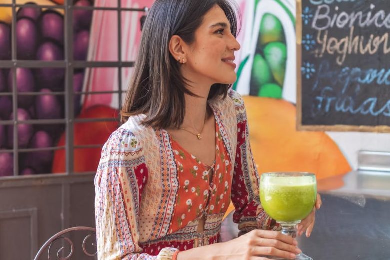 Woman holding a refreshing green juice in a lively café setting with colorful decor.